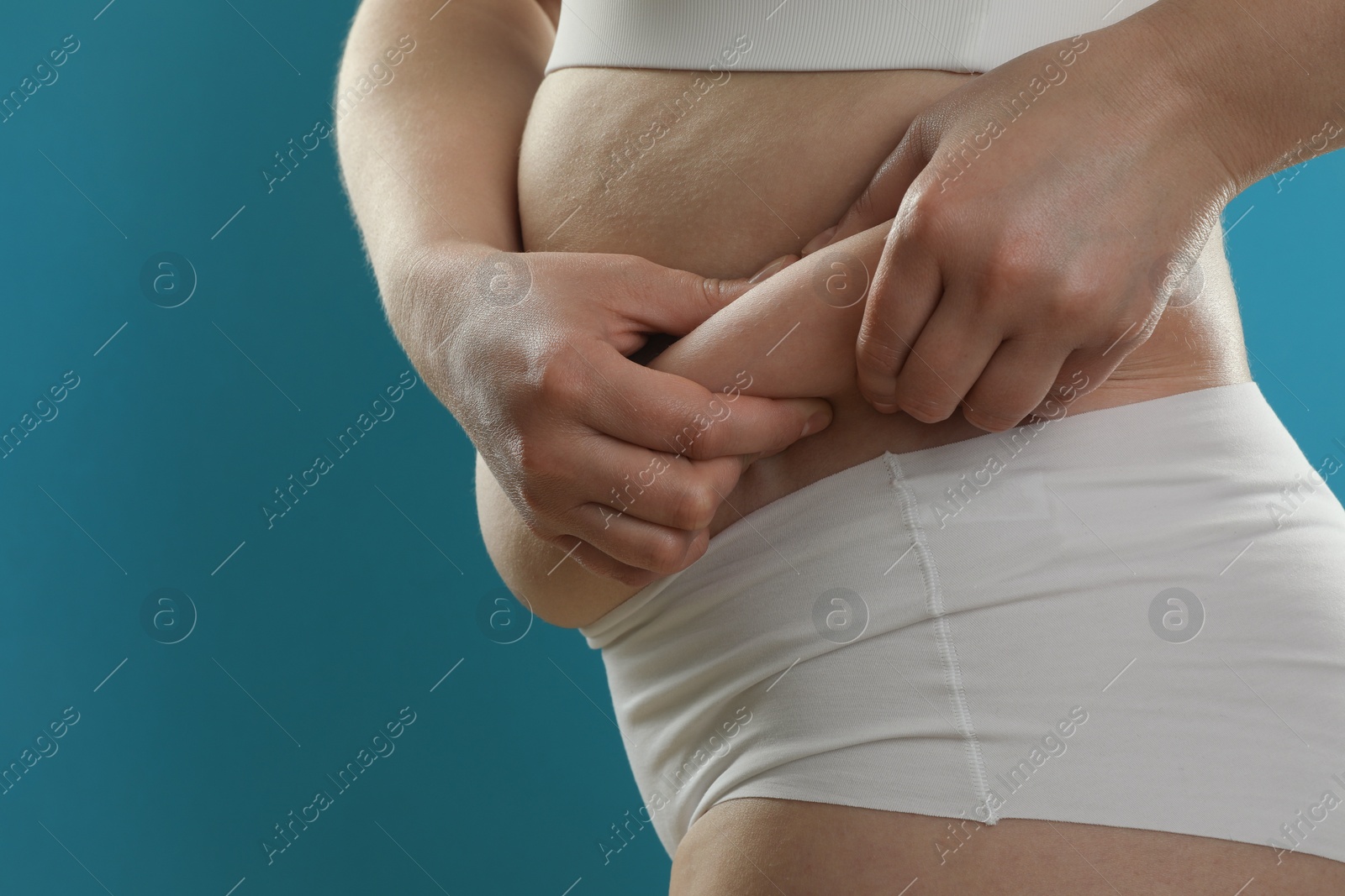 Photo of Woman touching belly fat on light blue background, closeup. Overweight problem