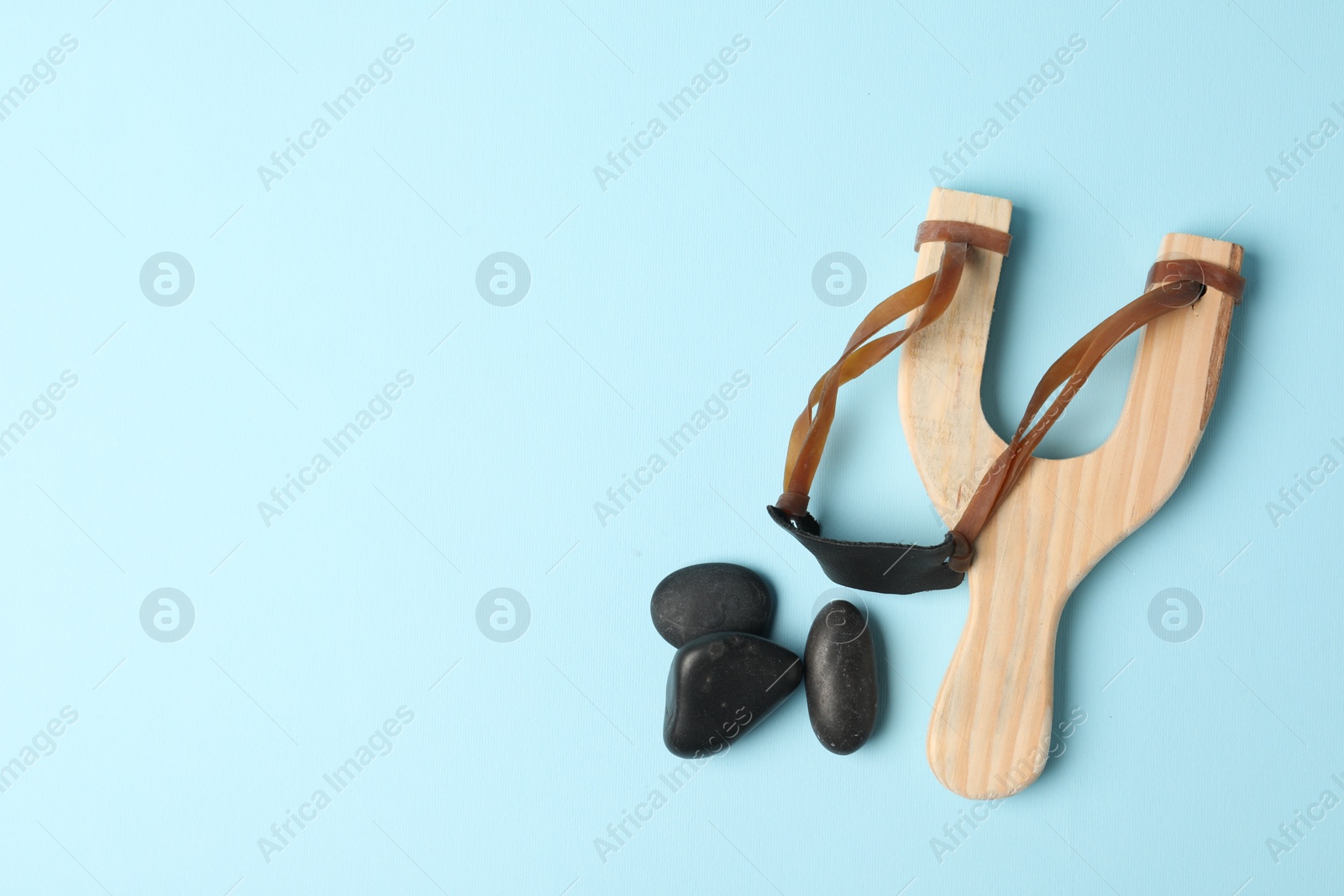 Photo of Wooden slingshot with stones on light blue background, flat lay. Space for text