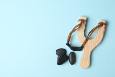 Wooden slingshot with stones on light blue background, flat lay. Space for text