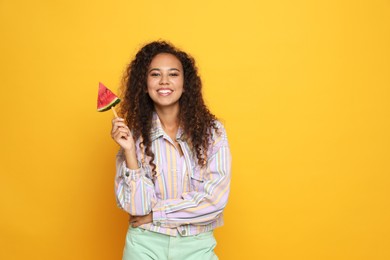 Photo of Beautiful young African American woman with piece of watermelon on yellow background. Space for text