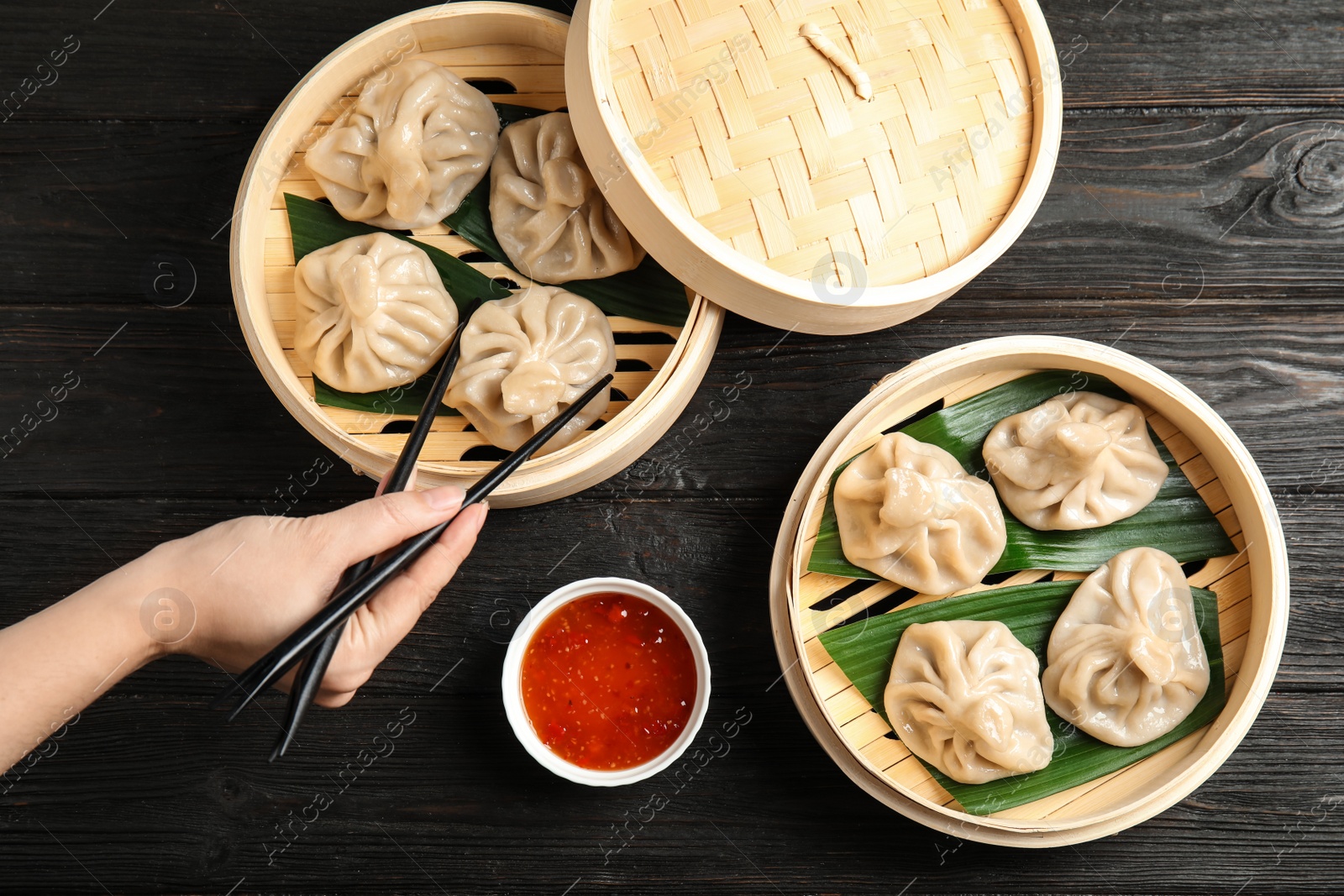 Photo of Woman cooking tasty baozi dumplings in bamboo steamers at table, top view