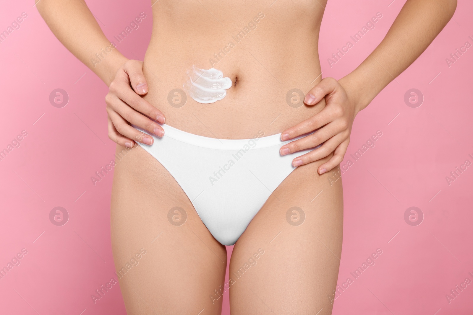 Photo of Woman with smear of body cream on belly against pink background, closeup