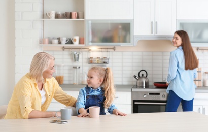 Photo of Young woman, her mother and daughter spending time in kitchen