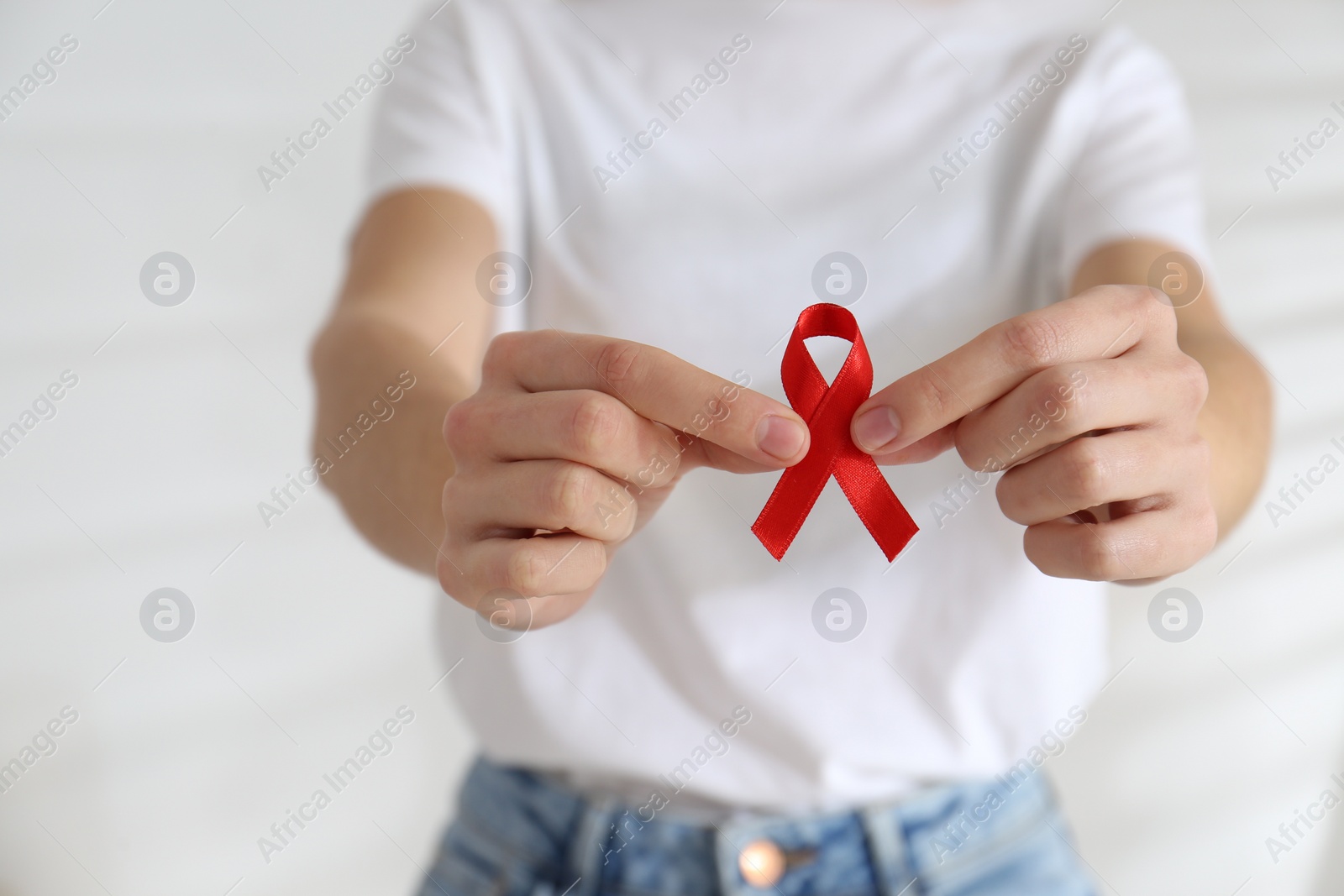 Photo of Woman holding red awareness ribbon on light background, closeup. World AIDS disease day