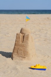 Photo of Beautiful sand castle with small Ukrainian flag and toy boat on beach near sea