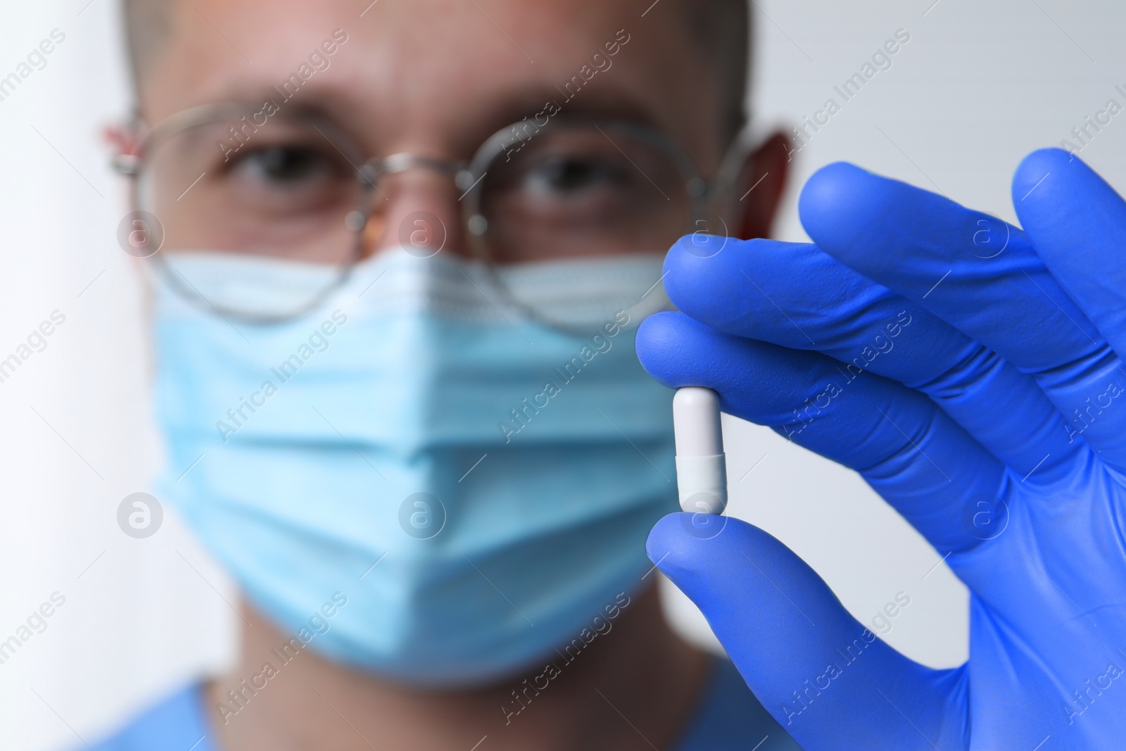 Photo of Doctor holding pill on light background, selective focus. Space for text