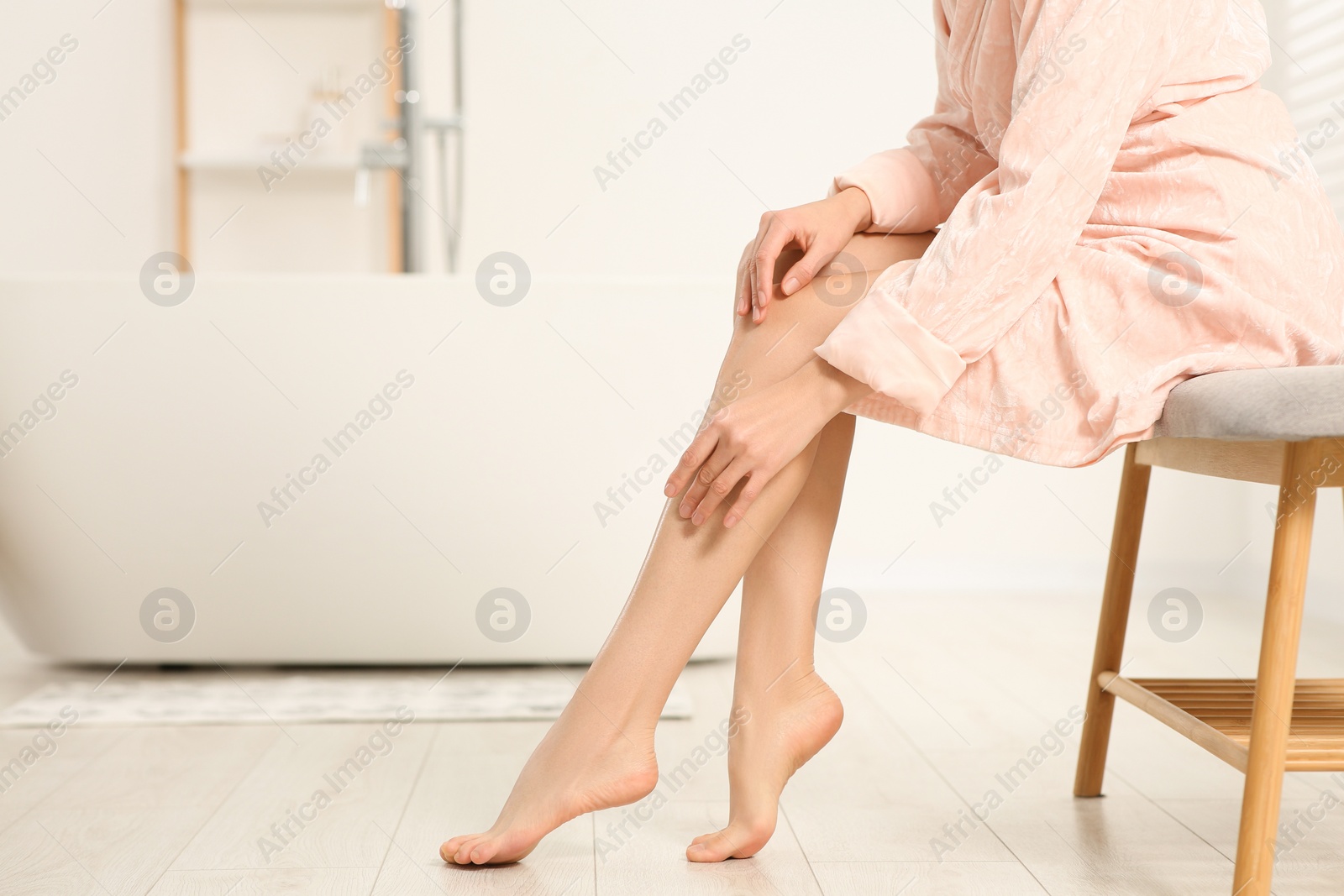 Photo of Woman in stylish bathrobe sitting on bench in bathroom, closeup. Space for text