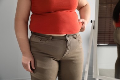 Photo of Overweight woman in tight shirt and trousers at home, closeup