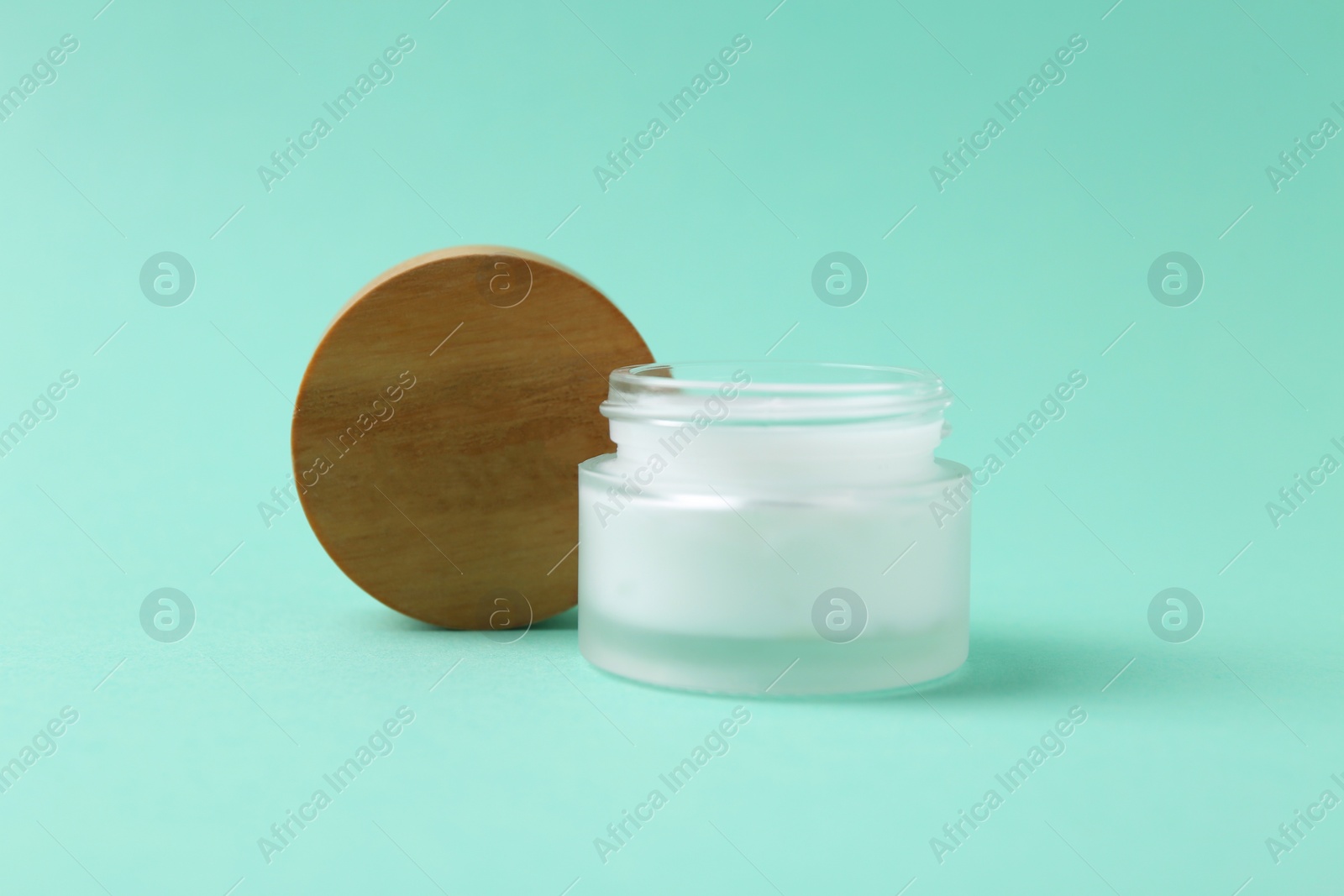 Photo of Moisturizing cream in open jar on turquoise background. Body care product