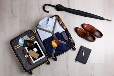 Photo of Packed suitcase with business trip stuff on wooden surface, flat lay