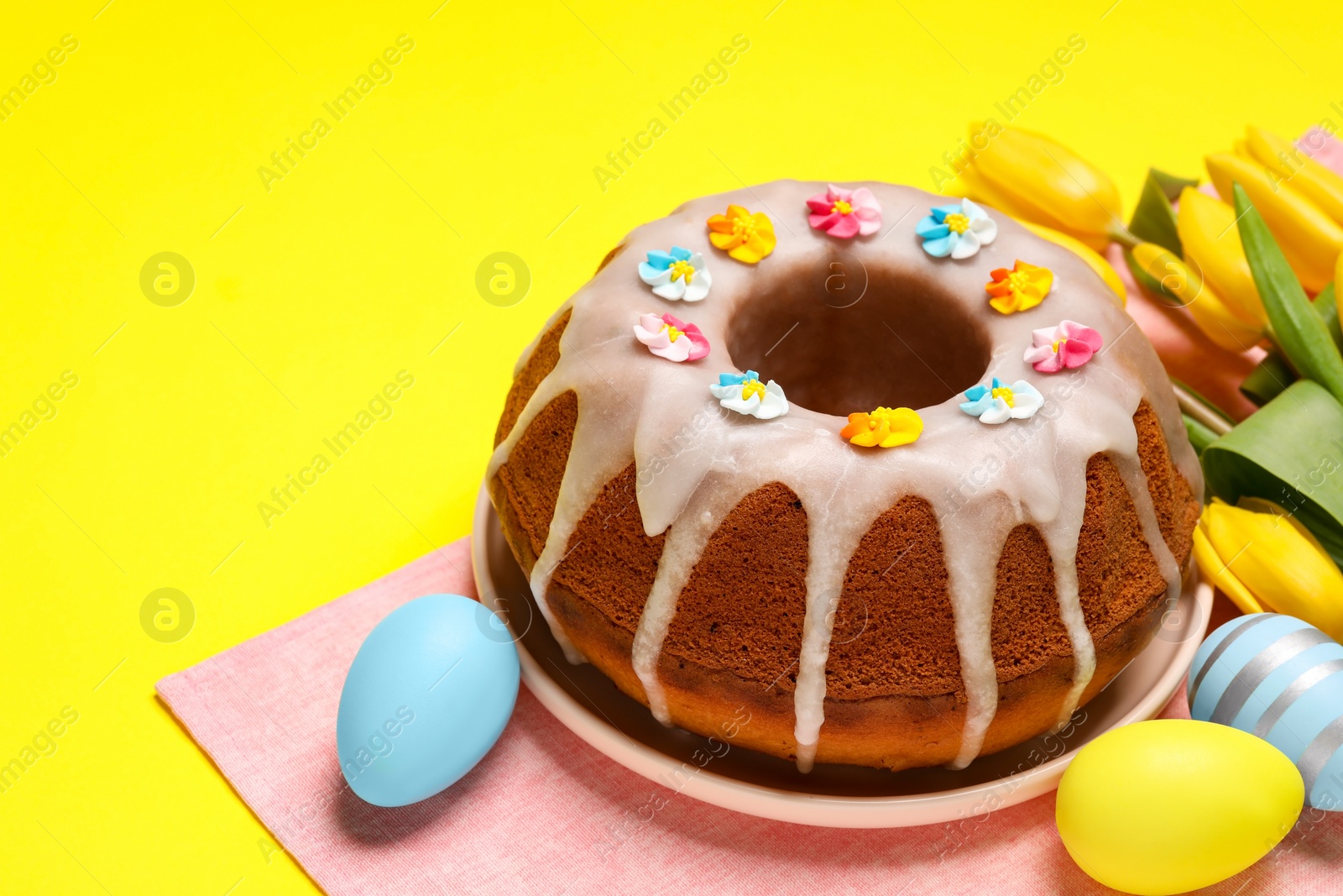 Photo of Delicious Easter cake decorated with sprinkles near beautiful tulips and painted eggs on yellow background. Space for text