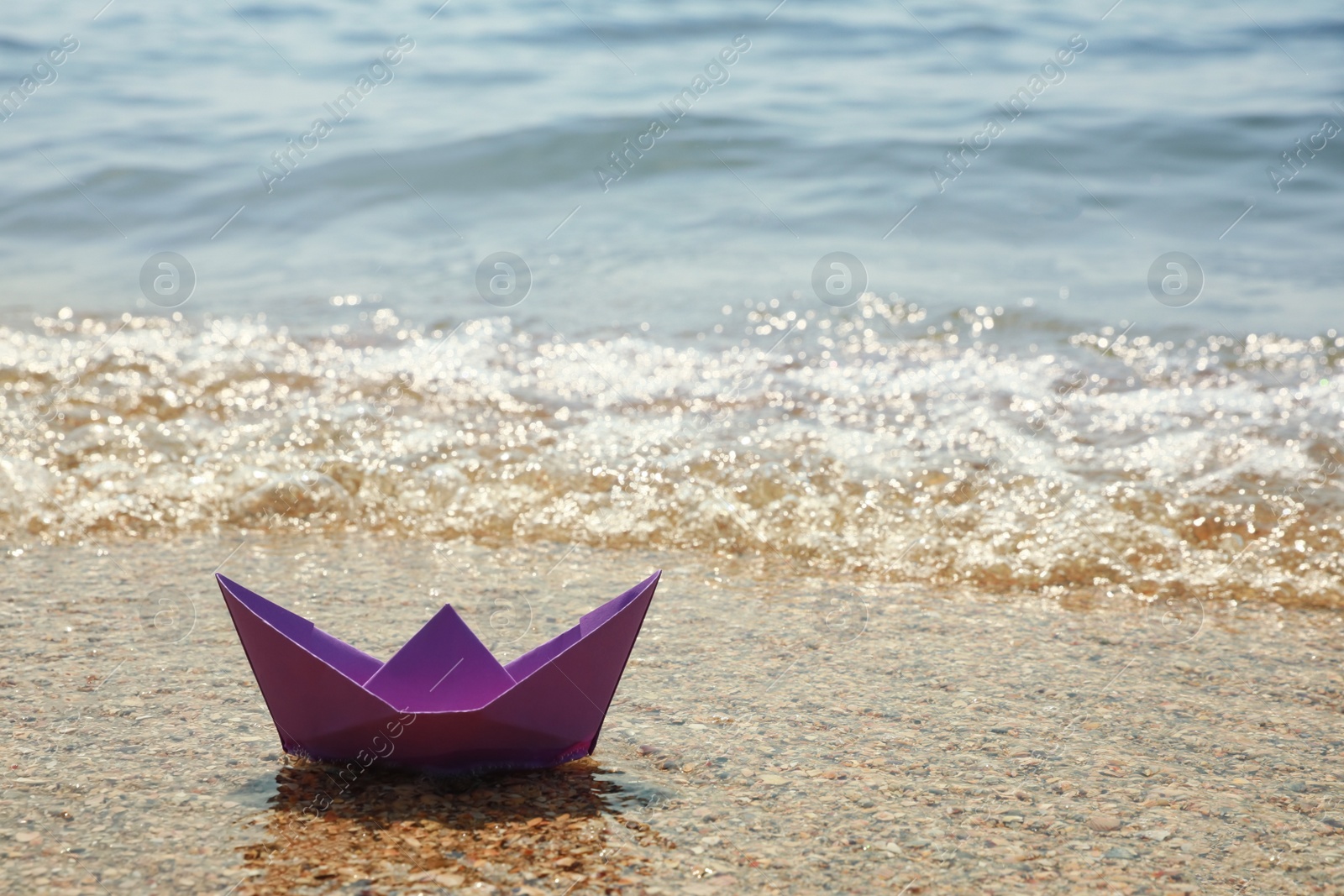 Photo of Purple paper boat near sea on sunny day, space for text