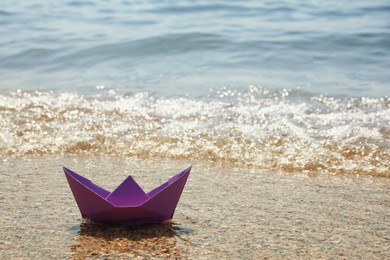 Photo of Purple paper boat near sea on sunny day, space for text