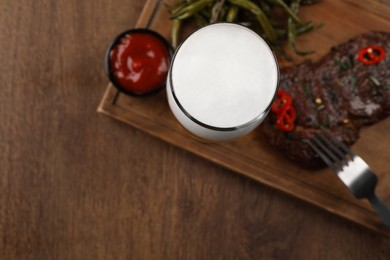 Photo of Glass of beer, delicious fried steak and sauce on wooden table, flat lay. Space for text