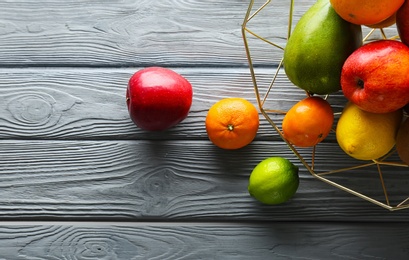 Photo of Metal basket with fresh tropical fruits on wooden background