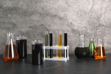 Photo of Beakers, flasks and test tubes with different types of oil on grey textured table, closeup. Space for text