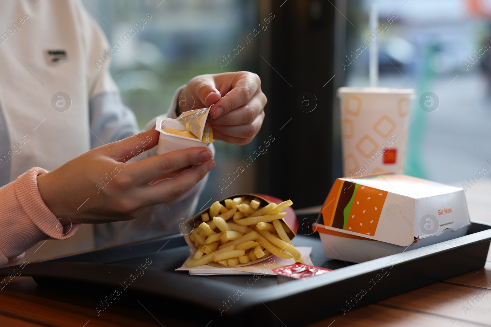 Photo of Lviv, Ukraine - September 26, 2023: Woman unpacking McDonald's sauce at wooden table in restaurant, closeup