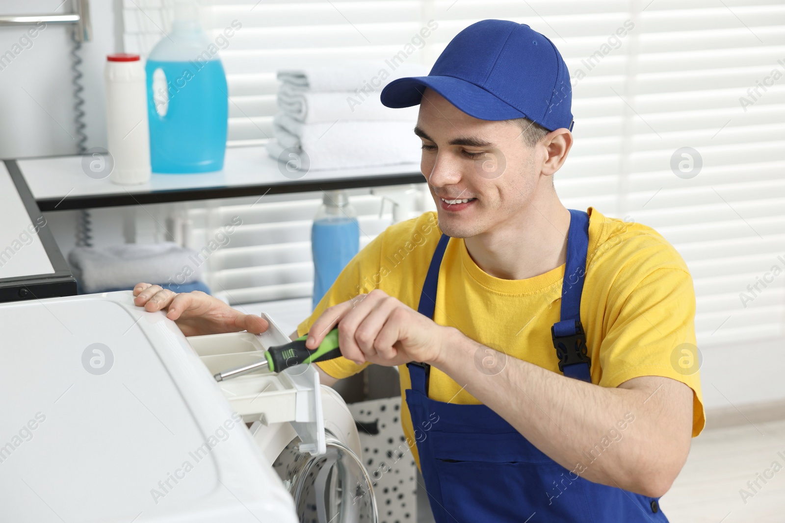 Photo of Smiling plumber with screwdriver repairing washing machine in bathroom