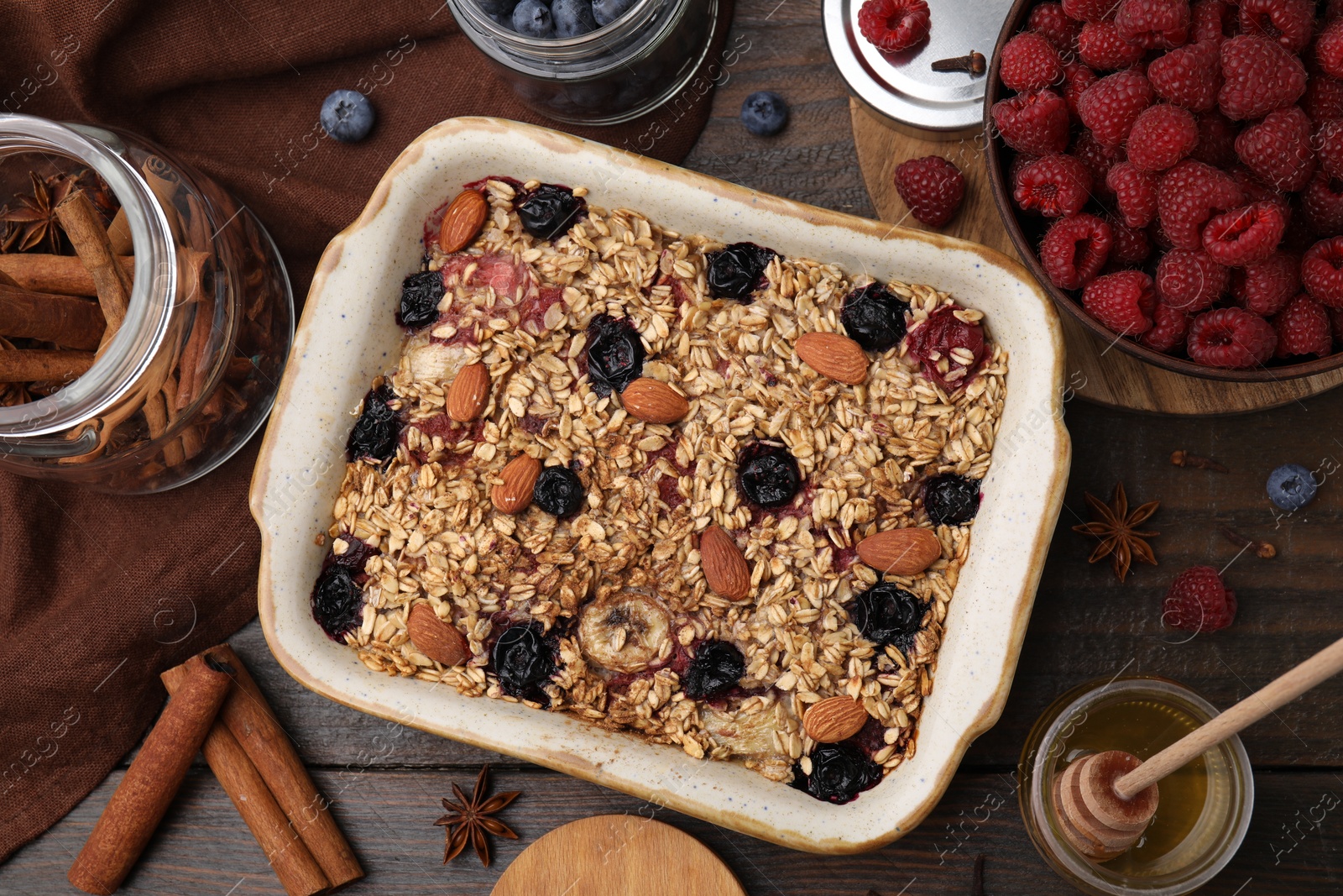 Photo of Tasty baked oatmeal with berries, almonds and spices in baking tray on wooden table, flat lay