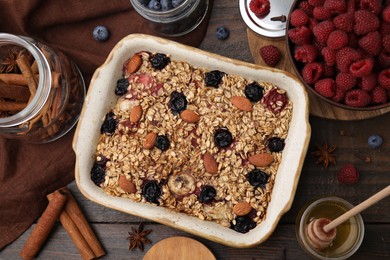 Photo of Tasty baked oatmeal with berries, almonds and spices in baking tray on wooden table, flat lay