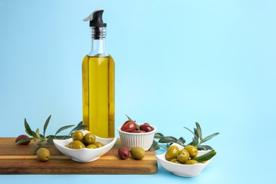 Photo of Bottle of oil, olives and tree twigs on light blue background, space for text