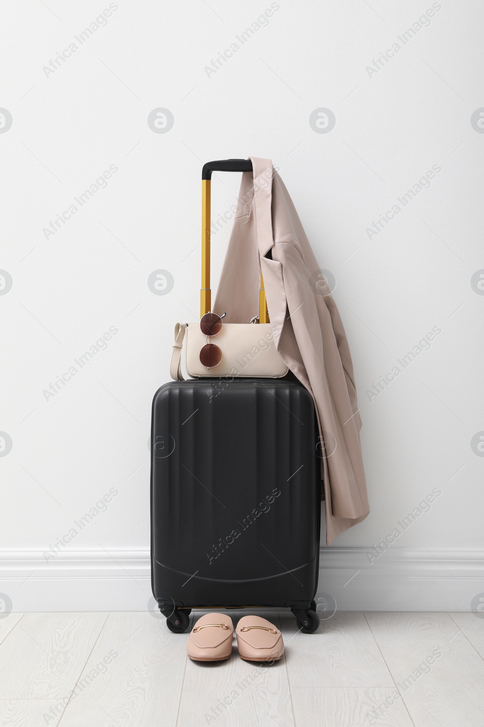 Photo of Suitcase packed for trip, shoes, jacket and accessories near white wall indoors