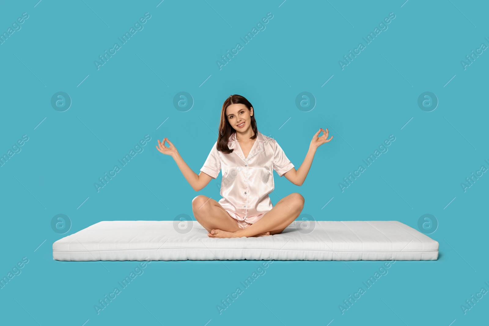 Photo of Young woman meditating on soft mattress against light blue background