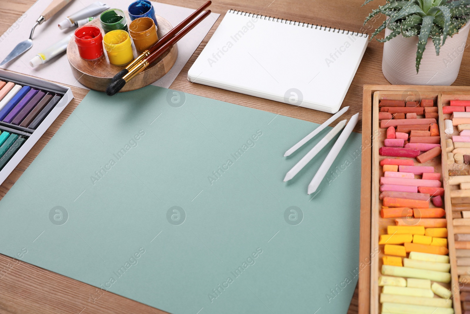 Photo of Blank sheet of paper, colorful chalk pastels and other drawing tools on wooden table. Modern artist's workplace