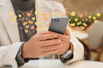 Long distance love. Man sending or receiving text message at table, closeup. Hearts flying out of device
