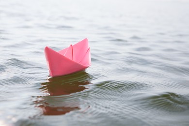 Photo of Pink paper boat on water surface, space for text