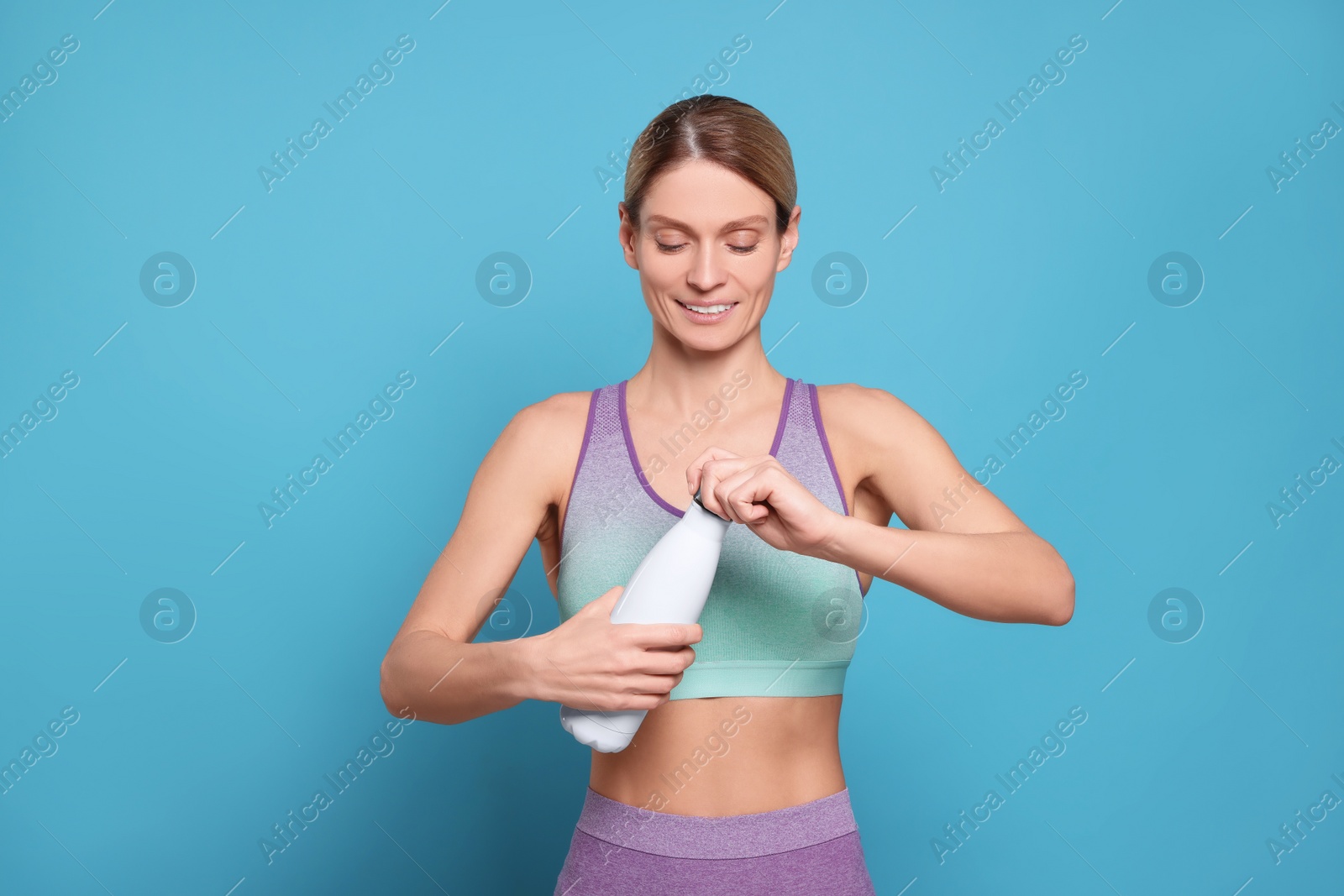 Photo of Sportswoman with thermo bottle on light blue background, space for text