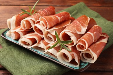 Photo of Rolled slices of delicious jamon with rosemary on wooden table, closeup