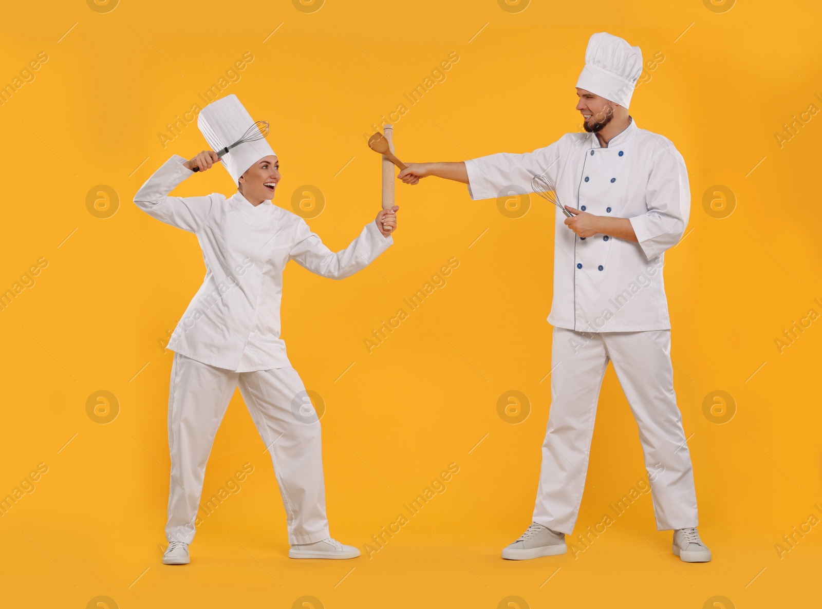 Photo of Happy professional confectioners in uniforms having fun on yellow background