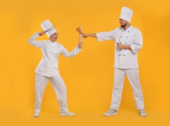 Photo of Happy professional confectioners in uniforms having fun on yellow background