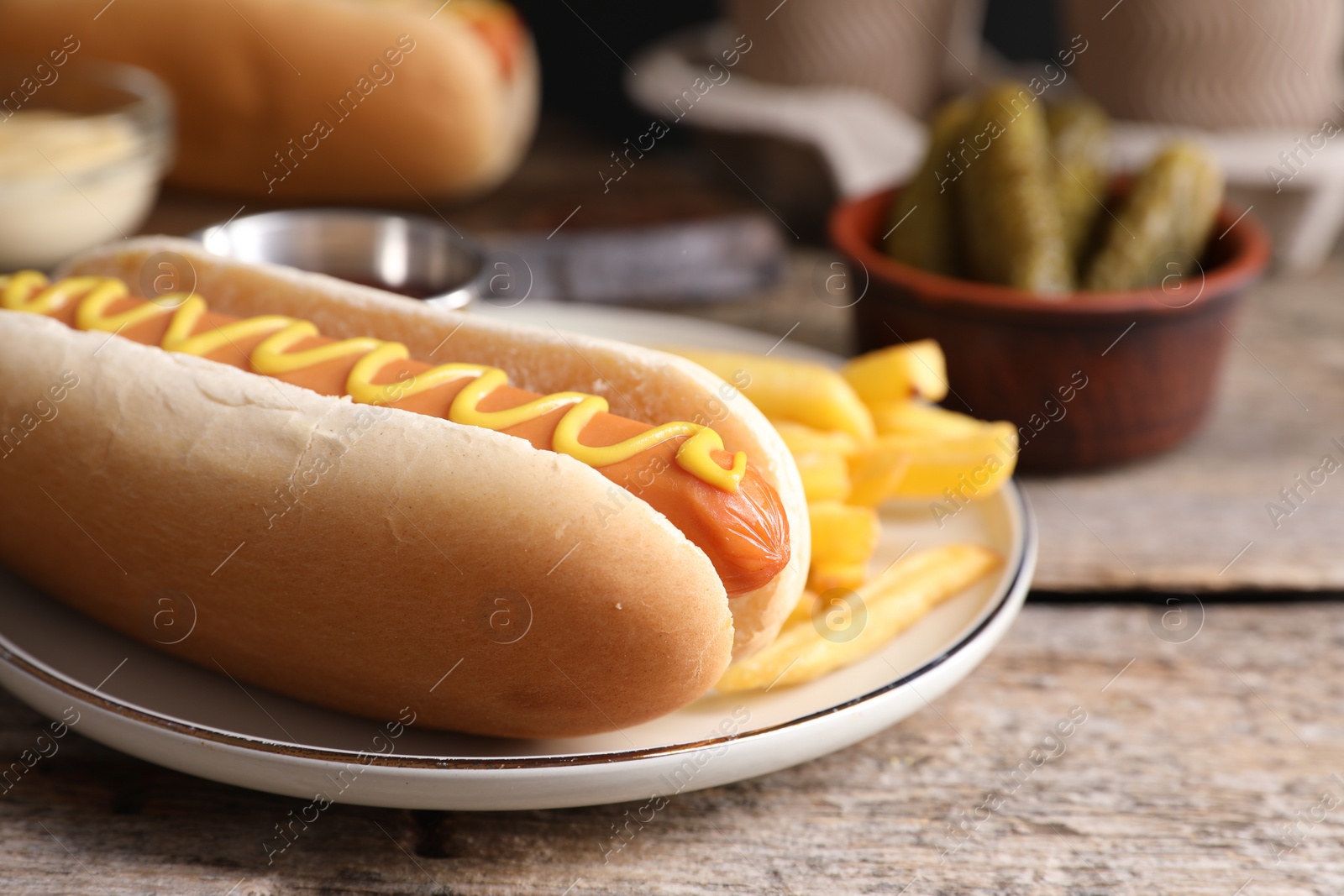 Photo of Delicious hot dog with mustard and French fries on wooden table, closeup