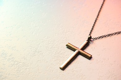 Cross with chain on textured table in color lights, closeup and space for text. Religion of Christianity