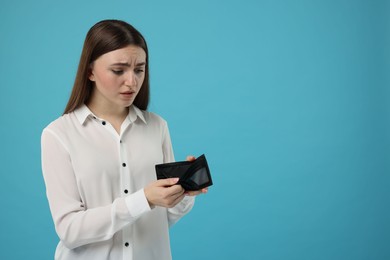 Photo of Sad woman showing empty wallet on light blue background, space for text