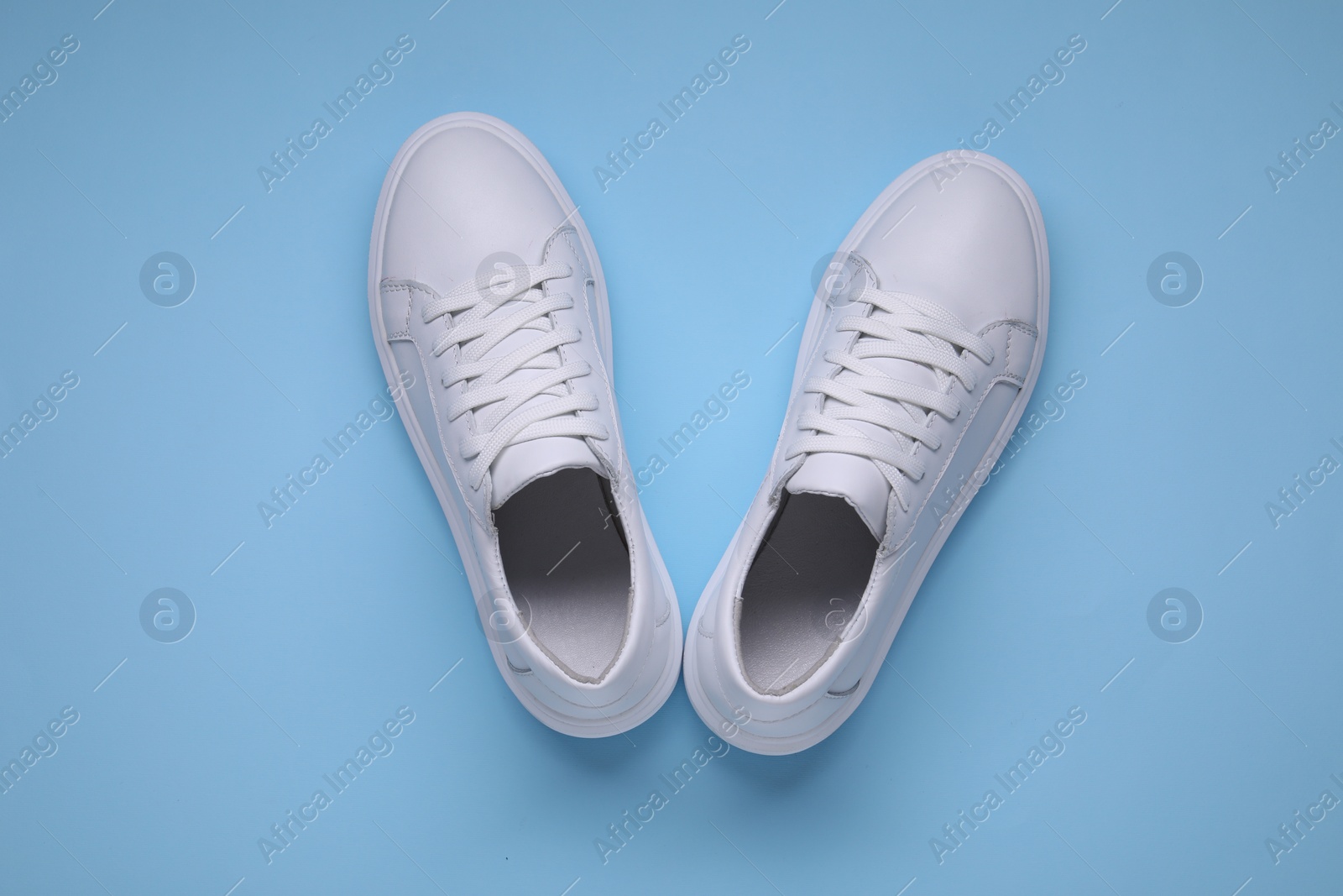 Photo of Pair of stylish white sneakers on light blue background, top view