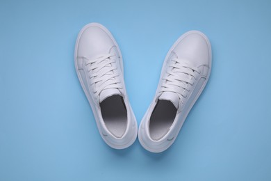 Pair of stylish white sneakers on light blue background, top view