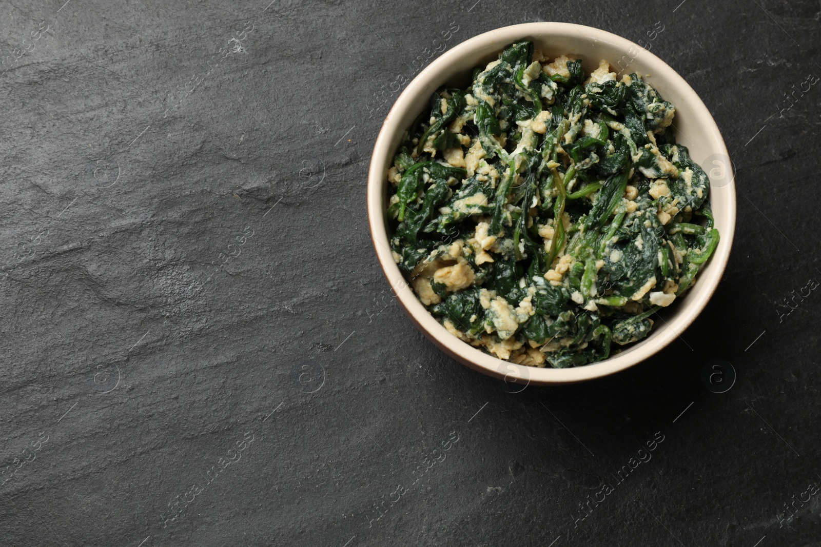 Photo of Tasty spinach dip with egg in bowl on black table, top view. Space for text