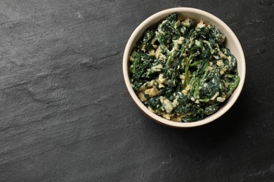 Photo of Tasty spinach dip with egg in bowl on black table, top view. Space for text