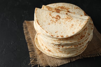 Photo of Stack of tasty homemade tortillas on black table, space for text