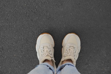 Photo of Woman in white sneakers standing on asphalt, top view