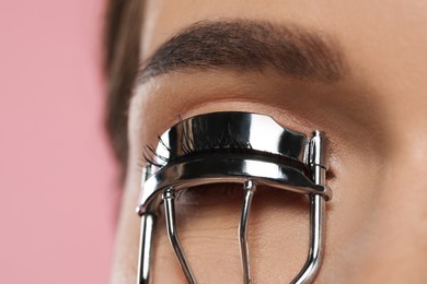 Woman using eyelash curler on pink background, closeup