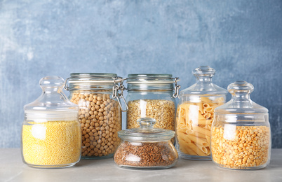 Photo of Jars with different cereals on grey marble table against light blue background