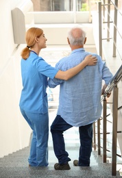 Photo of Nurse assisting elderly man on stairs indoors