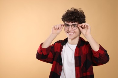 Portrait of happy teenage boy wearing glasses on beige background. Space for text