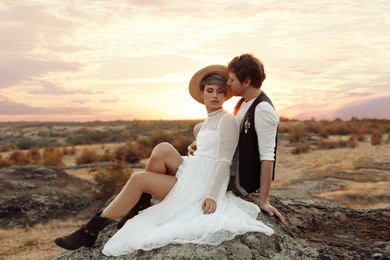 Photo of Happy newlyweds sitting on rock at sunset