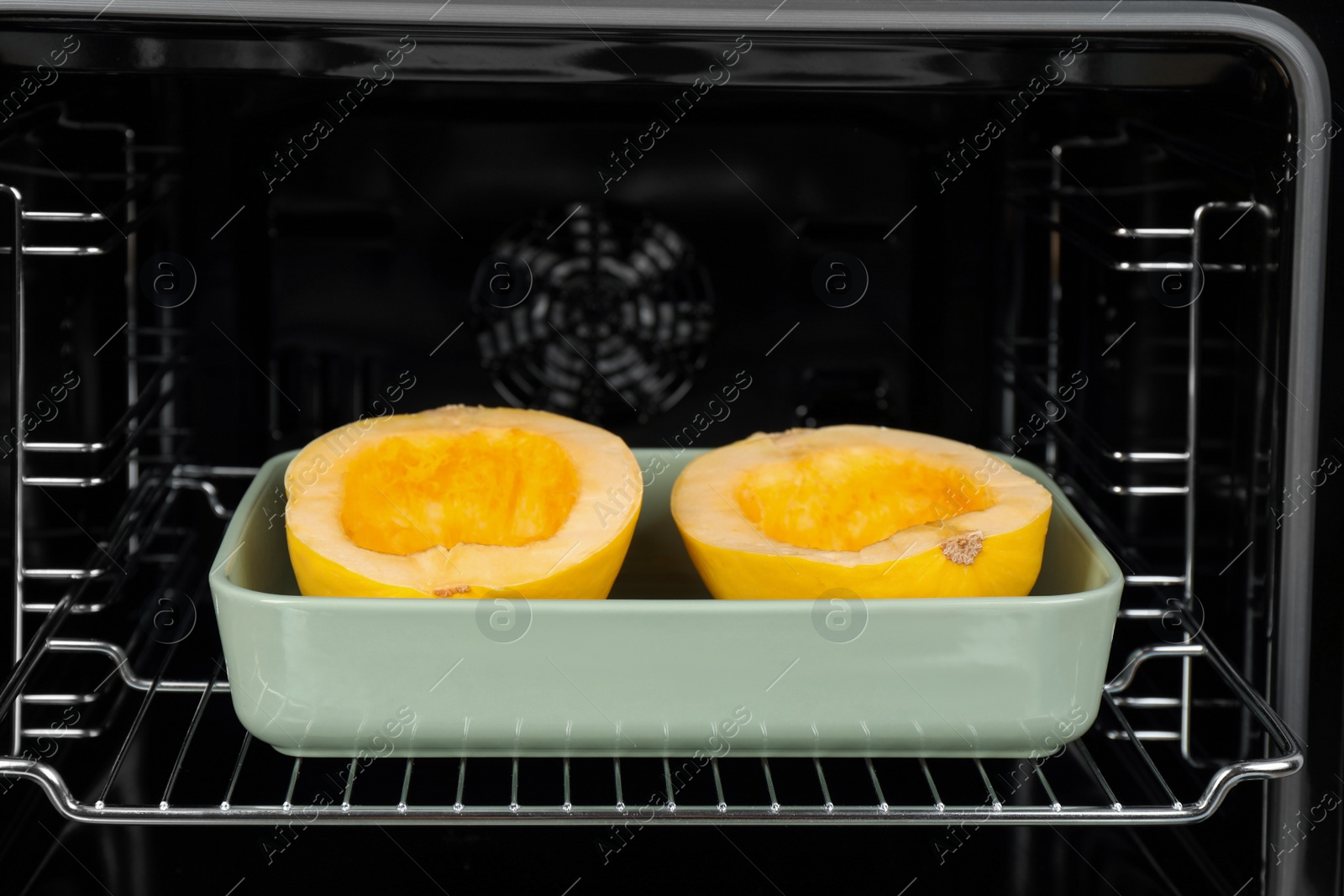 Photo of Baking dish with halves of fresh spaghetti squash in oven