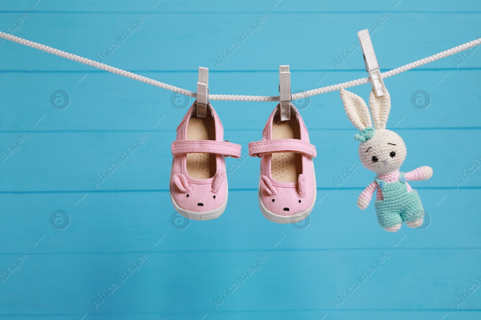 Photo of Cute baby shoes and crochet toy drying on washing line against light blue wooden wall